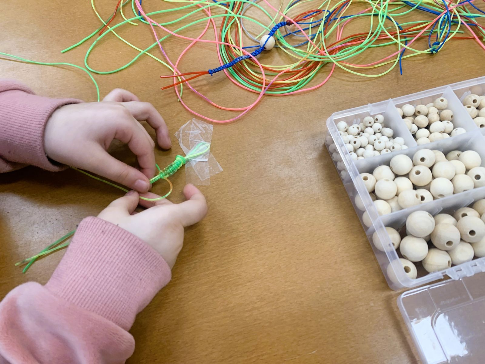 Zdjęcie przedstawiające ręce dziecka wykonującego ozdoby z gumowych kabelków.
