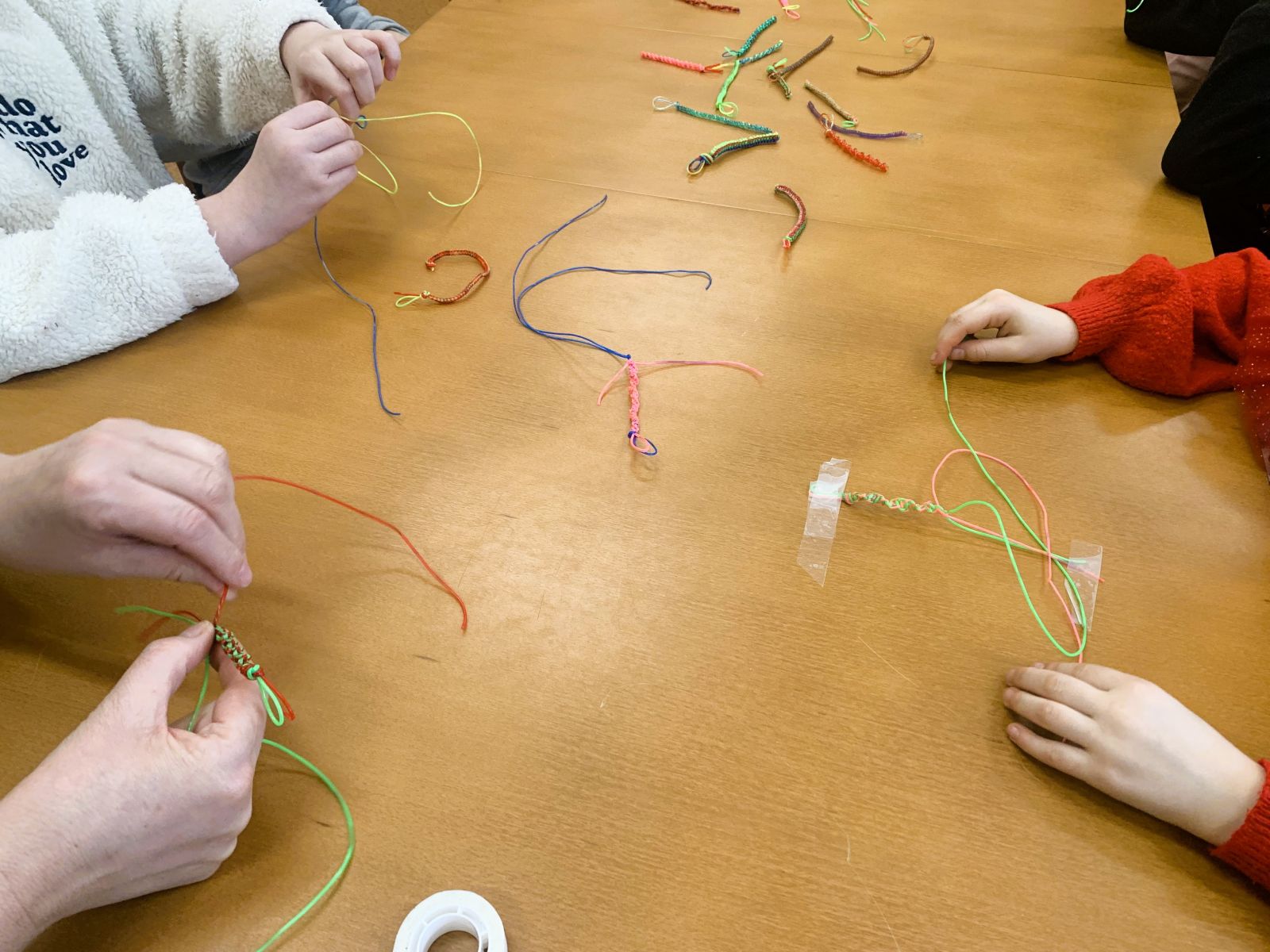 Zdjęcie przedstawiające ręce dzieci wykonujących ozdoby z gumowych kabelków.