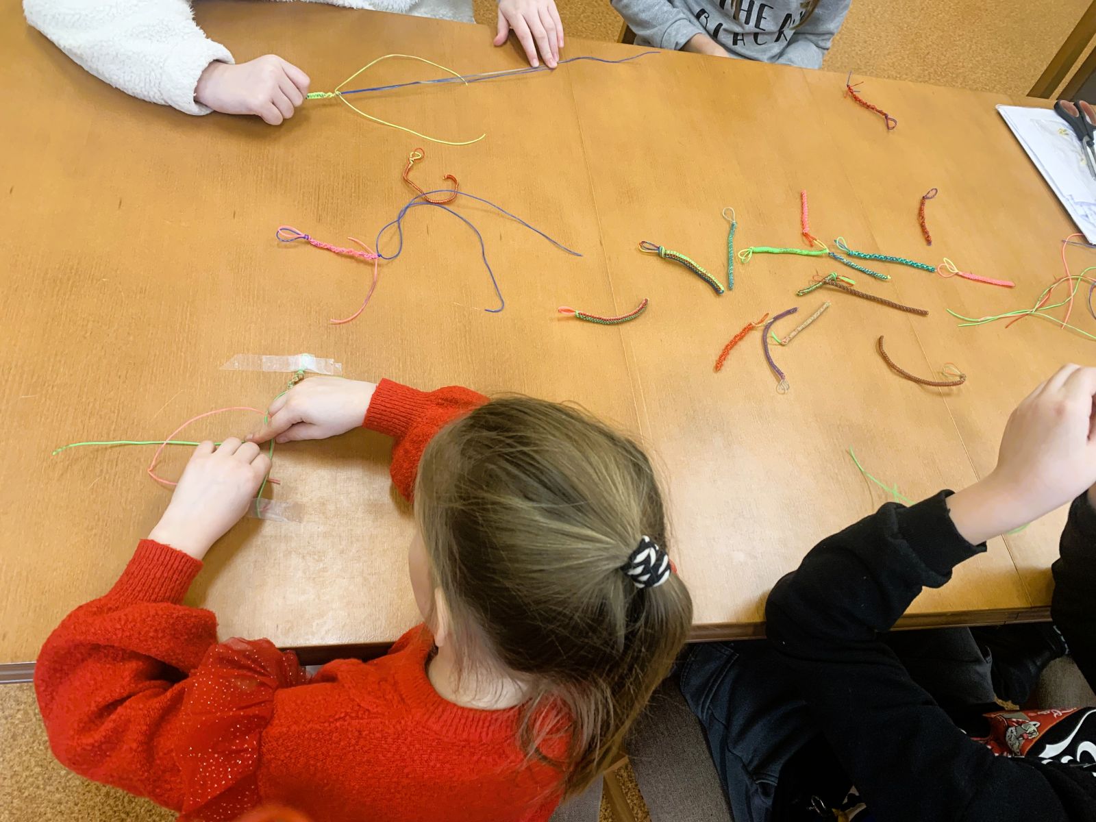 Zdjęcie przedstawiające dzieci wykonujące ozdoby z gumowych kabelków.