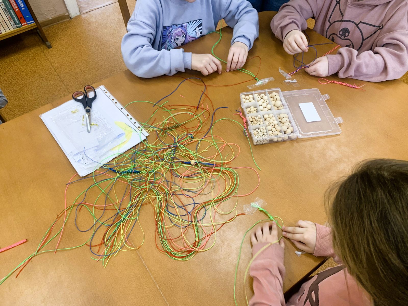 Zdjęcie przedstawiające dzieci wykonujące ozdoby z gumowych kabelków.