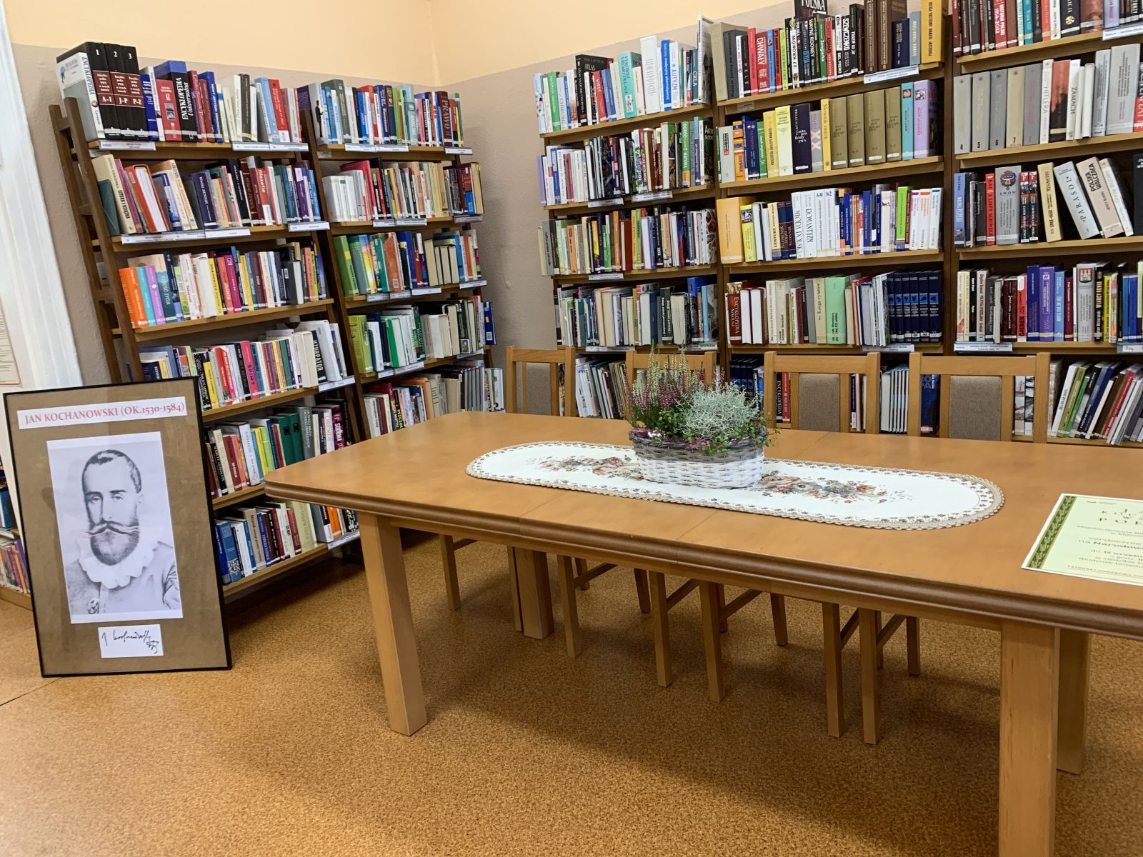 Stół i krzesła na tle regałów bibliotecznych.