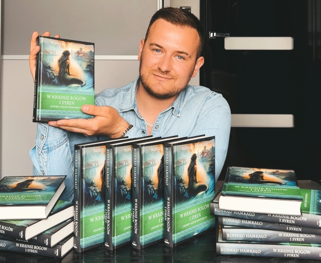 Fotografia przedstawiająca pisarza prezentującego swoje książki.